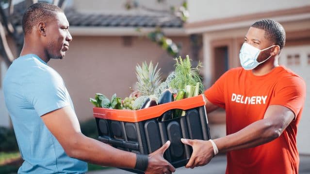 A Bounty Barn courier handing a crate of fresh produce to a customer