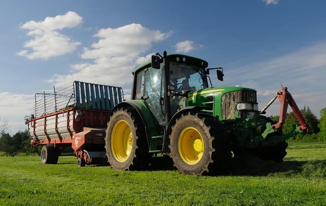 A green tractor pulling a trailer across a grassy field